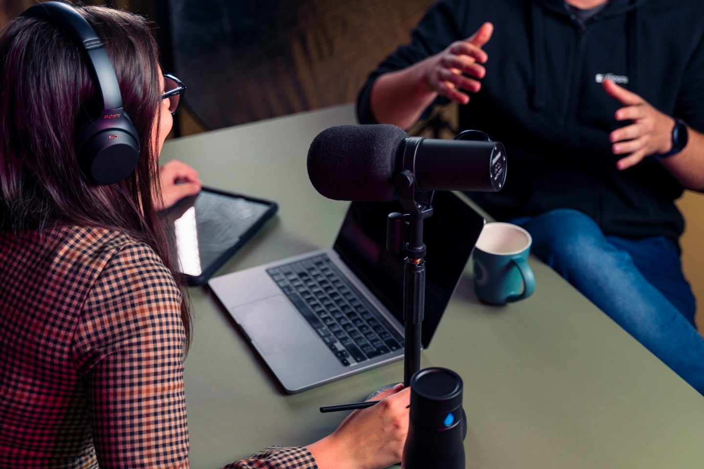 Dos personas grabando un podcast con micrófonos y ordenadores portátiles.