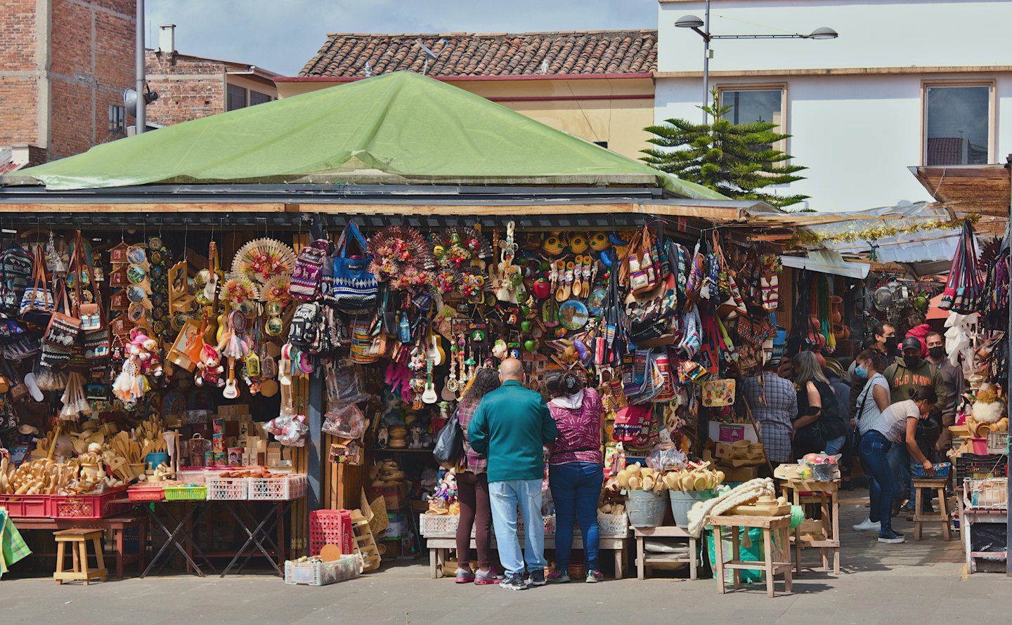 Compradores curiosean coloridas artesanías en un puesto de mercado al aire libre.