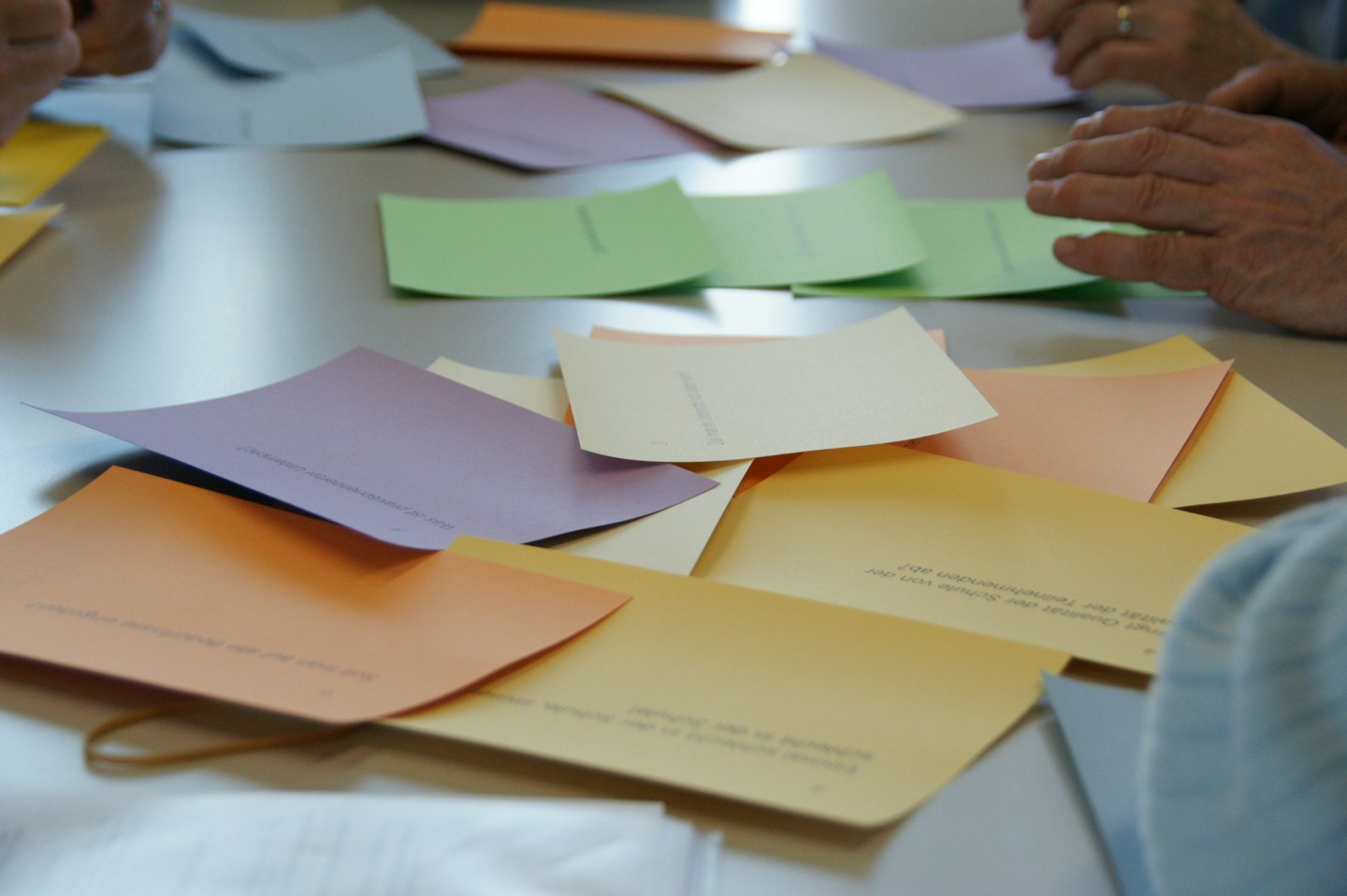 Personas organizan tarjetas con texto en alemán sobre una mesa de taller.