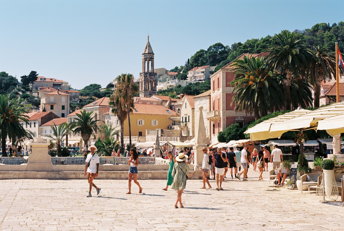 Gente disfrutando de un día soleado en una animada plaza de un pueblo mediterráneo.