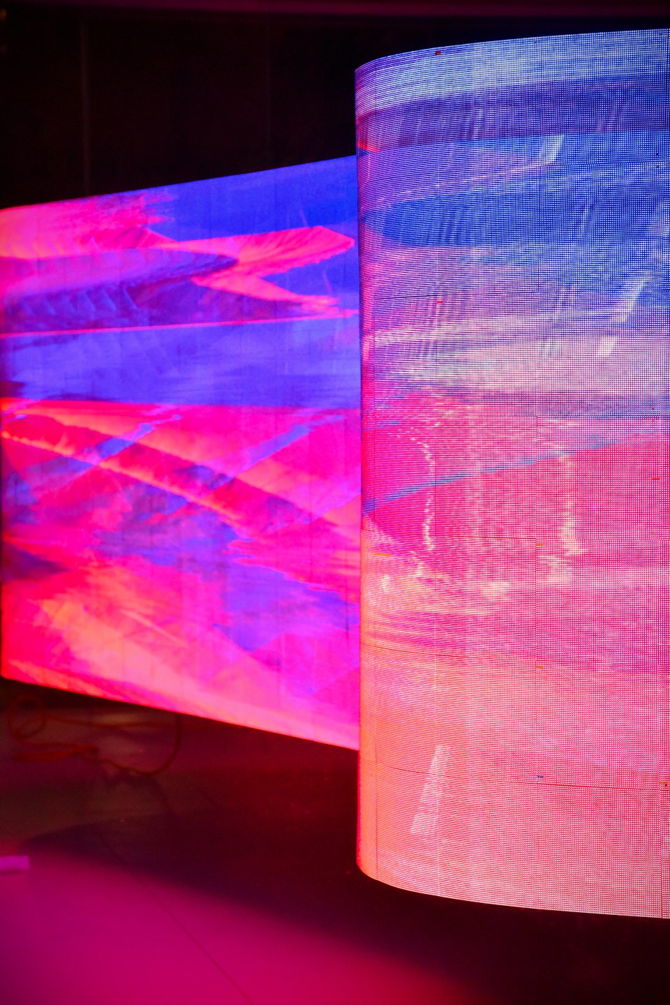 Dos pantallas LED curvas y grandes muestran vibrantes patrones digitales abstractos.