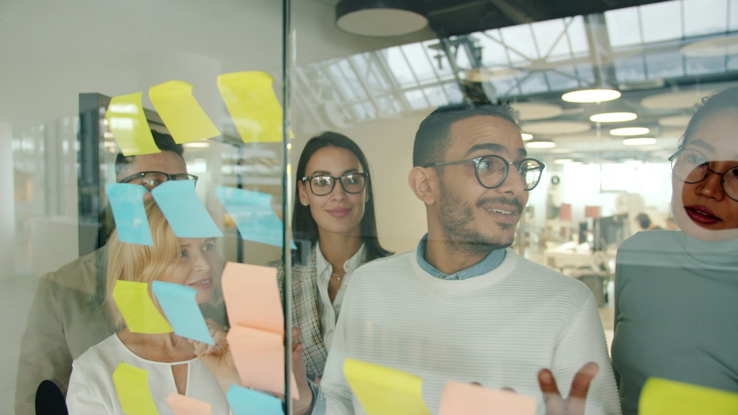Equipo diverso intercambiando ideas con notas adhesivas en un cristal.